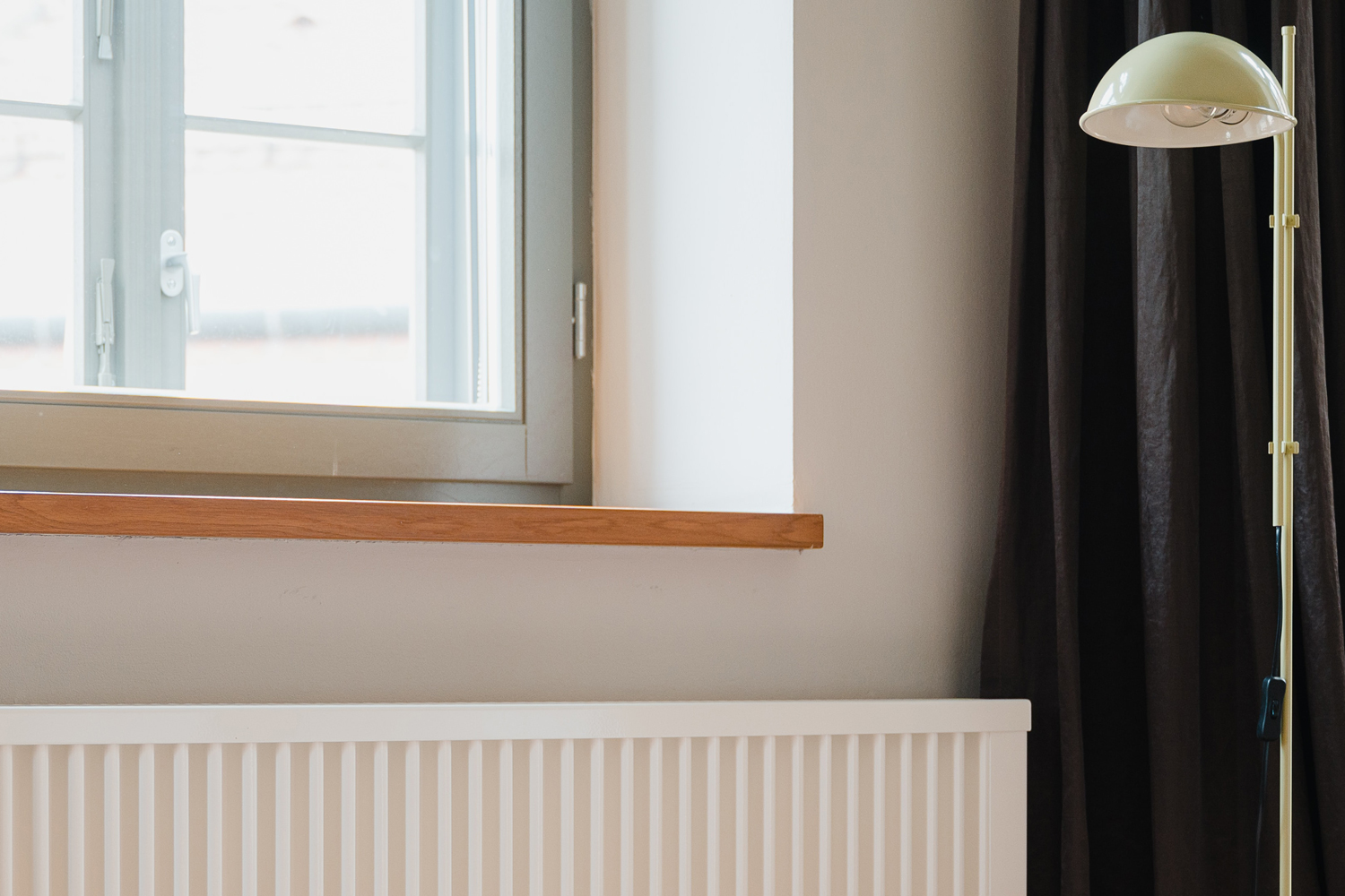 Blick auf ein Fenster, darunter ein weißer Heizkörper. Am rechten Bildrand ist eine Stehlampe zu sehen.
