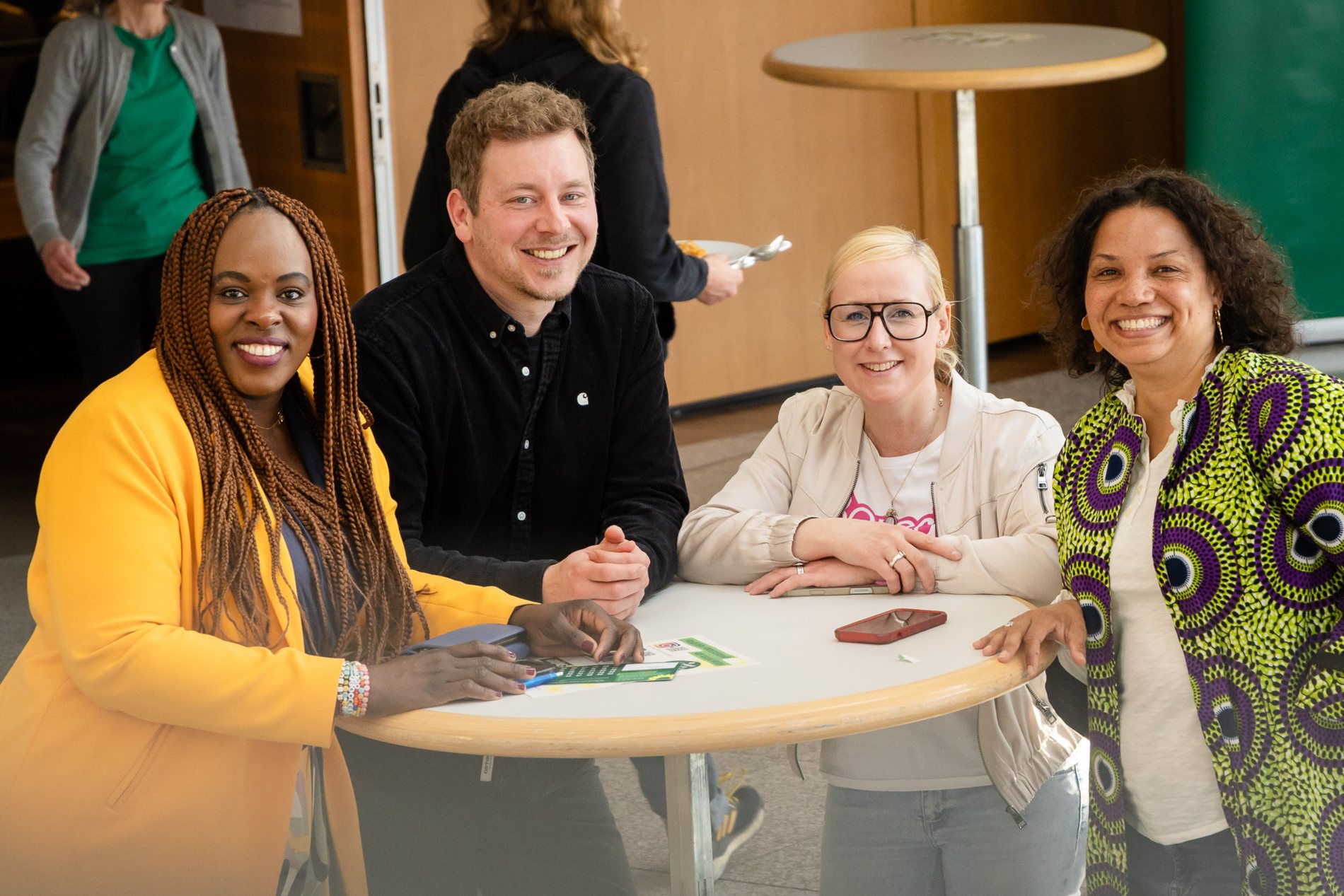 Vier Menschen an einem Stehtisch lächeln in die Kamera.