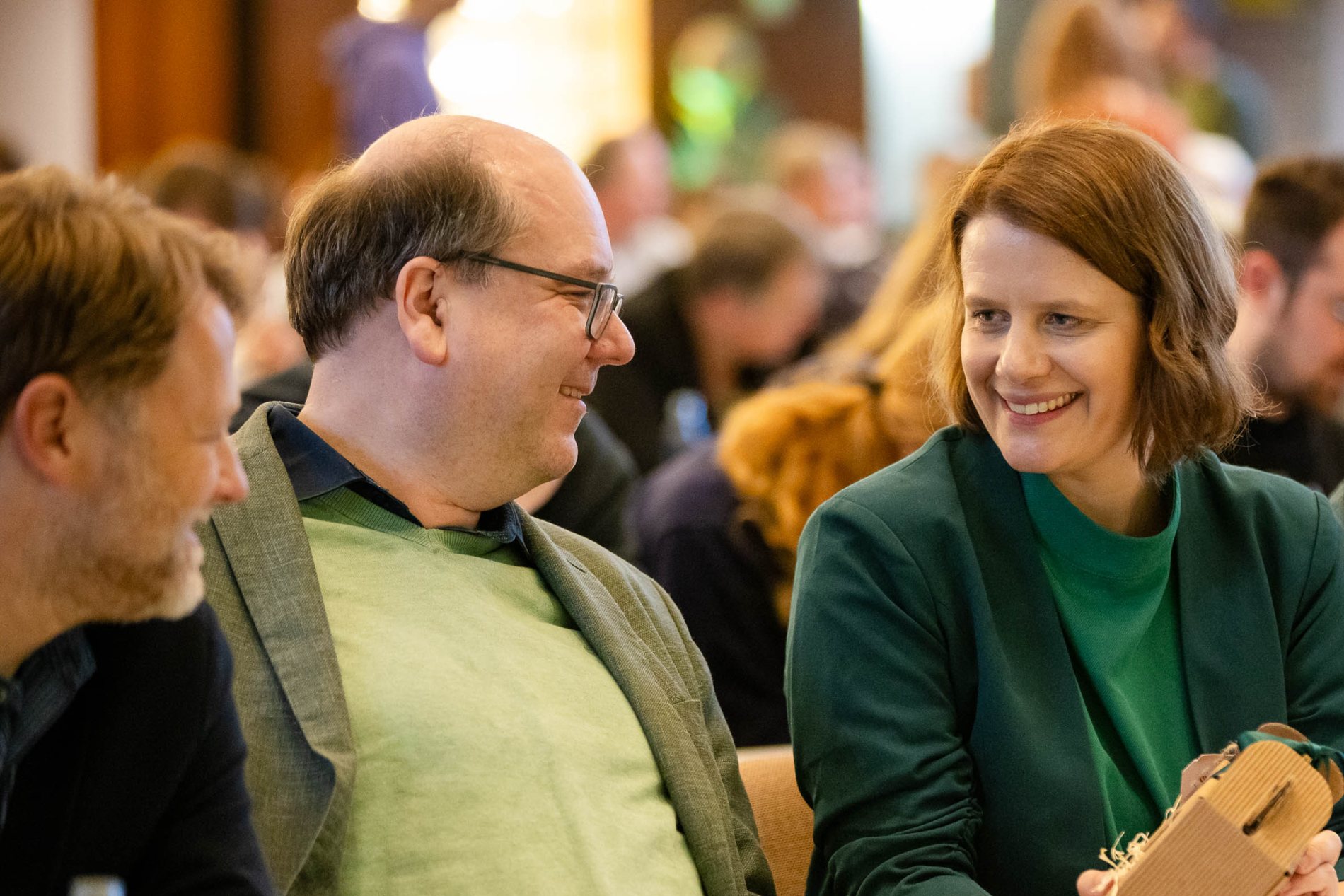 Drei Menschen sitzen nebeneinander und lächeln sich an.
